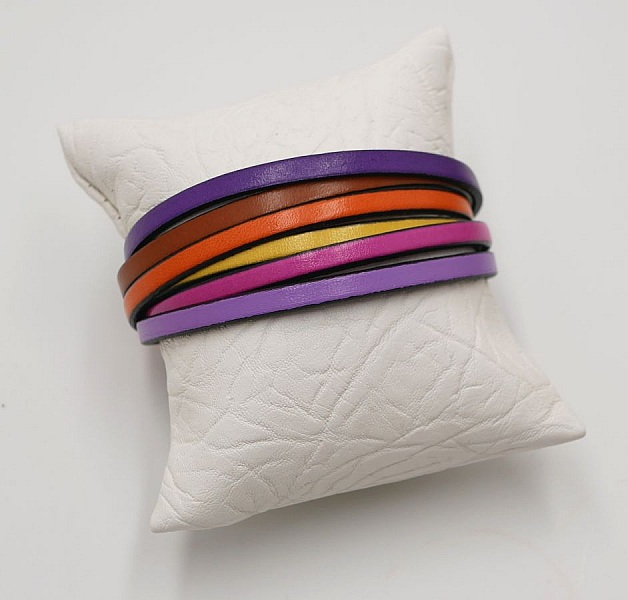 Bracelet manchette multi-cuirs aux couleurs vives sur coussin blanc.