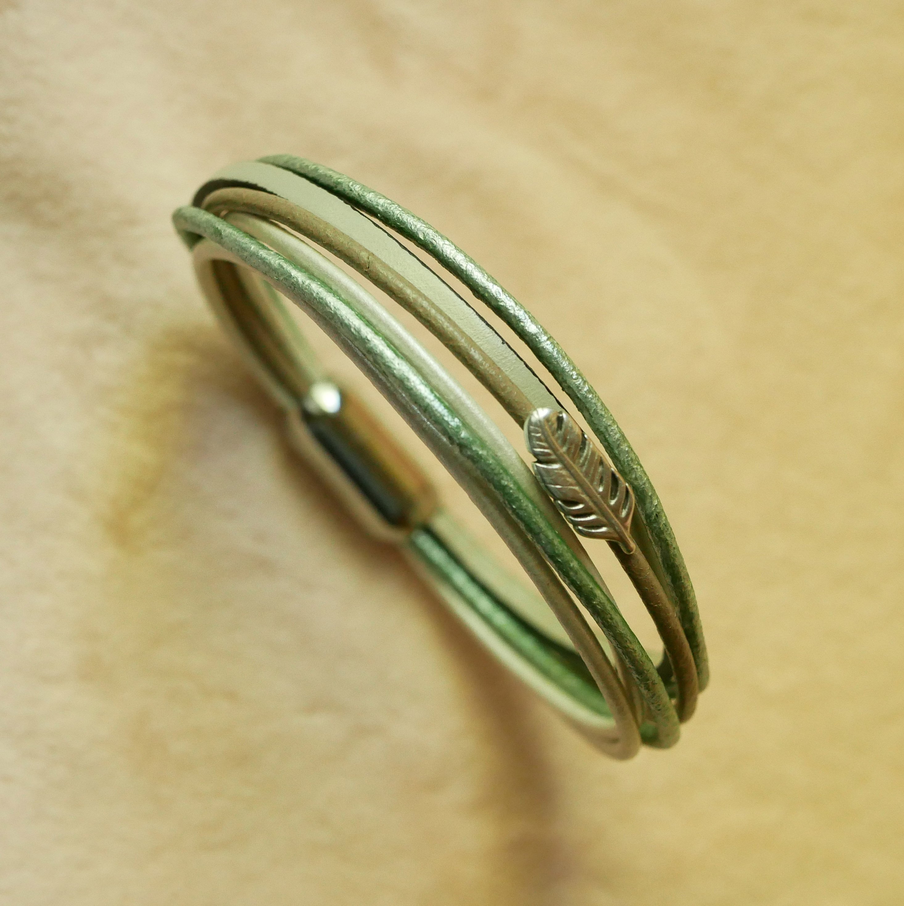 Bracciale in pelle multipla nei toni del beige, del verde chiaro e del perlato, decorato con una piccola piuma