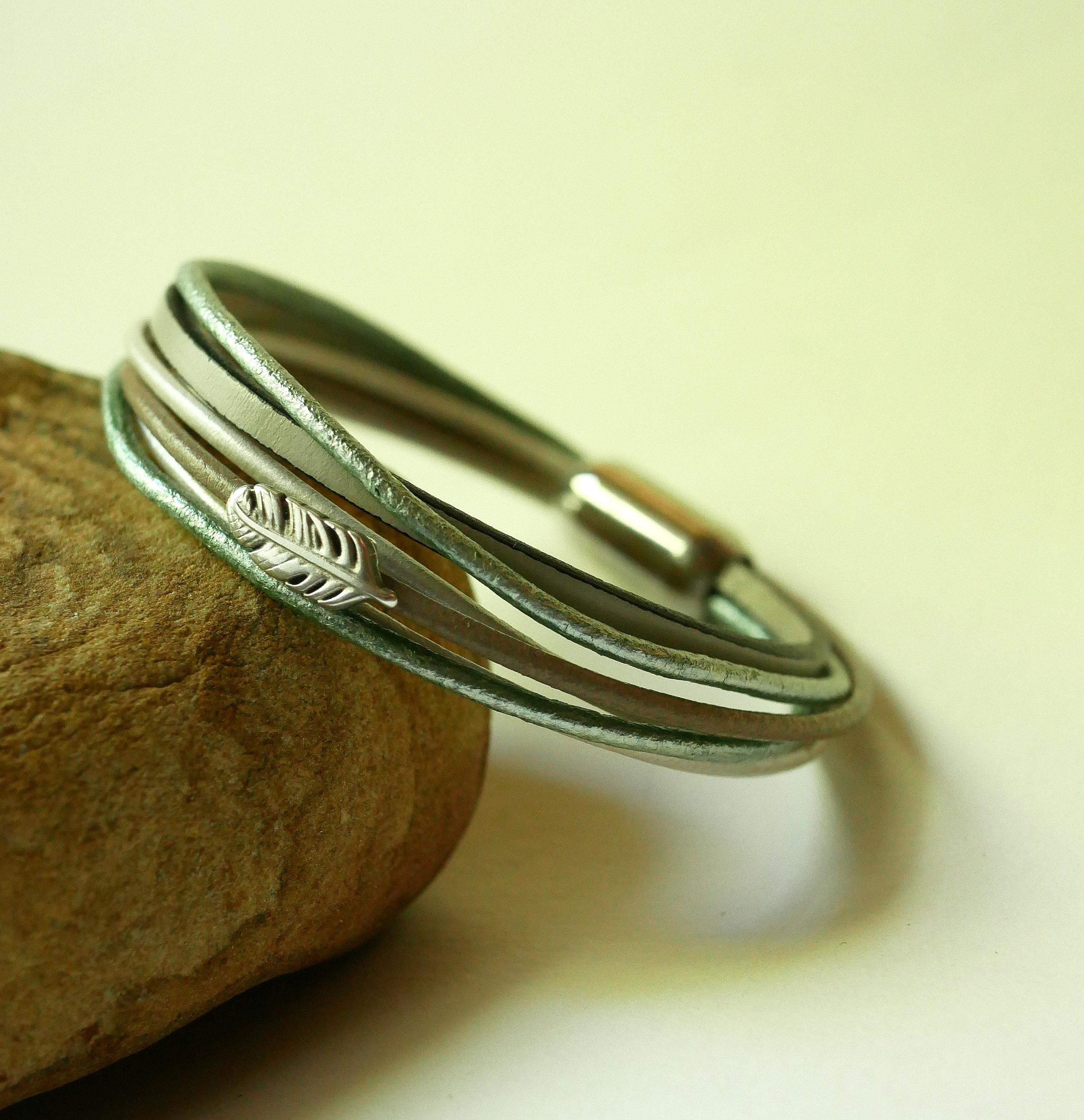 Bracciale in pelle multipla nei toni del beige, del verde chiaro e del perlato, decorato con una piccola piuma