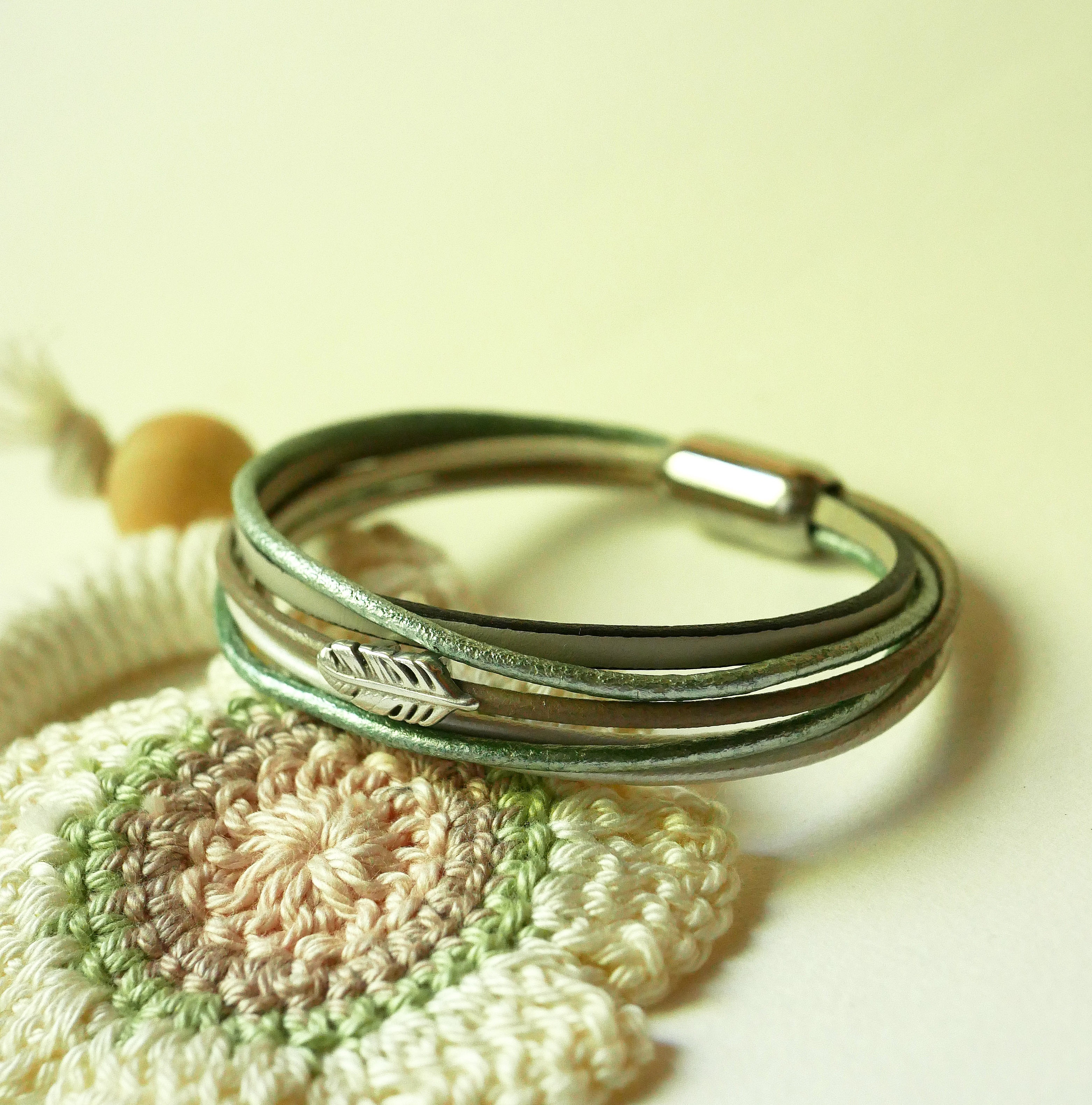 Bracciale in pelle multipla nei toni del beige, del verde chiaro e del perlato, decorato con una piccola piuma