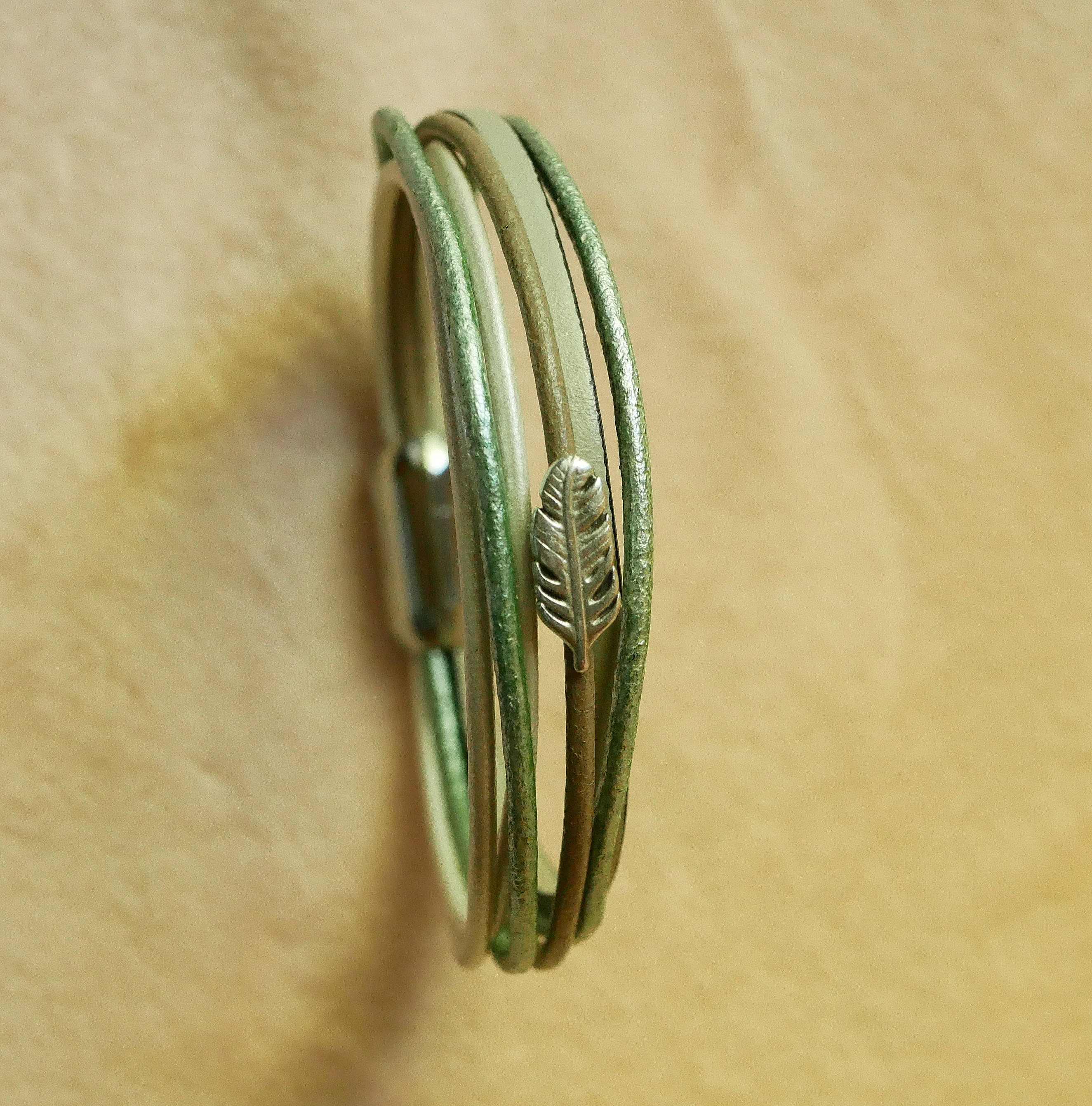 Bracciale in pelle multipla nei toni del beige, del verde chiaro e del perlato, decorato con una piccola piuma