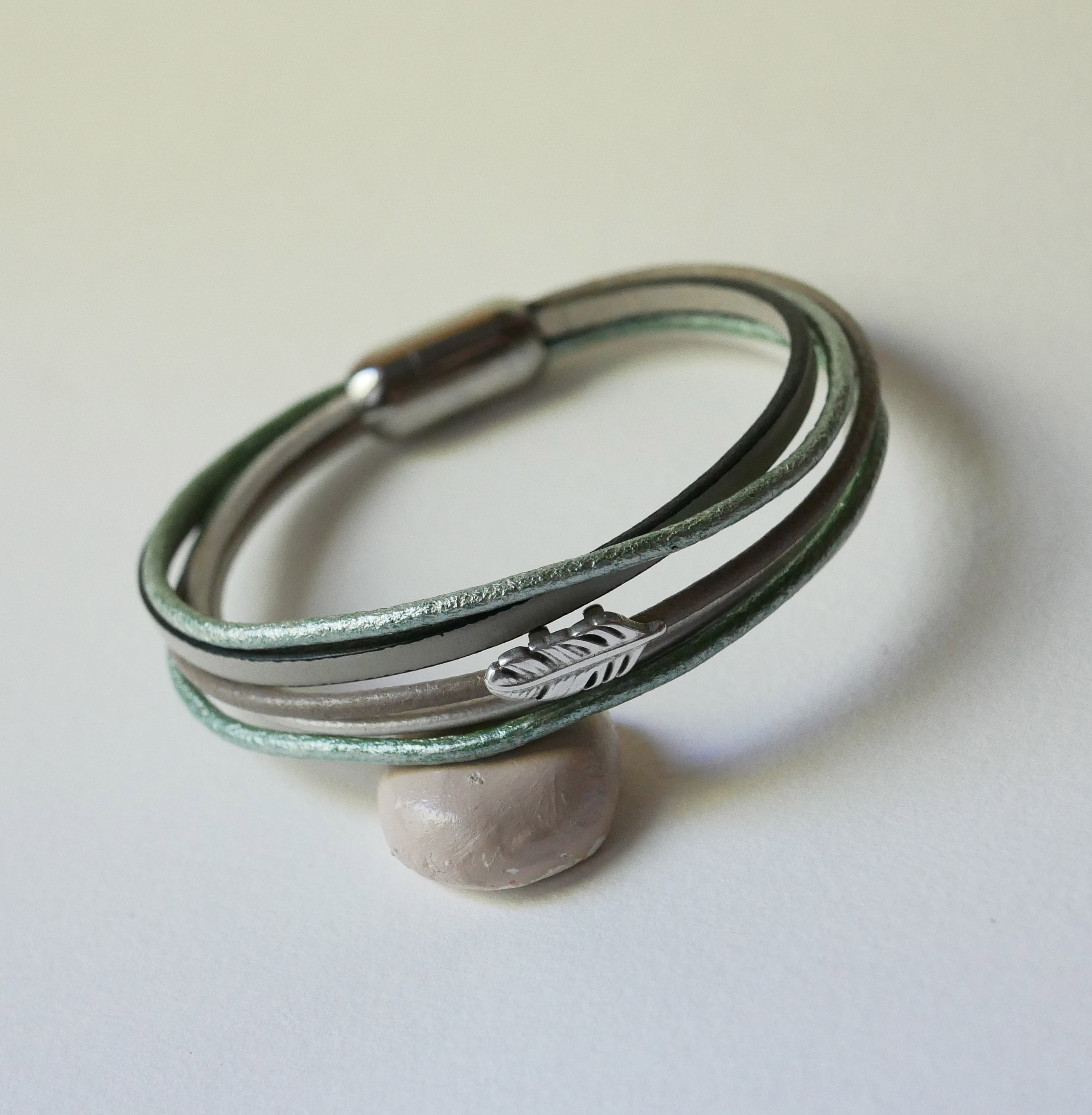 Bracciale in pelle multipla nei toni del beige, del verde chiaro e del perlato, decorato con una piccola piuma