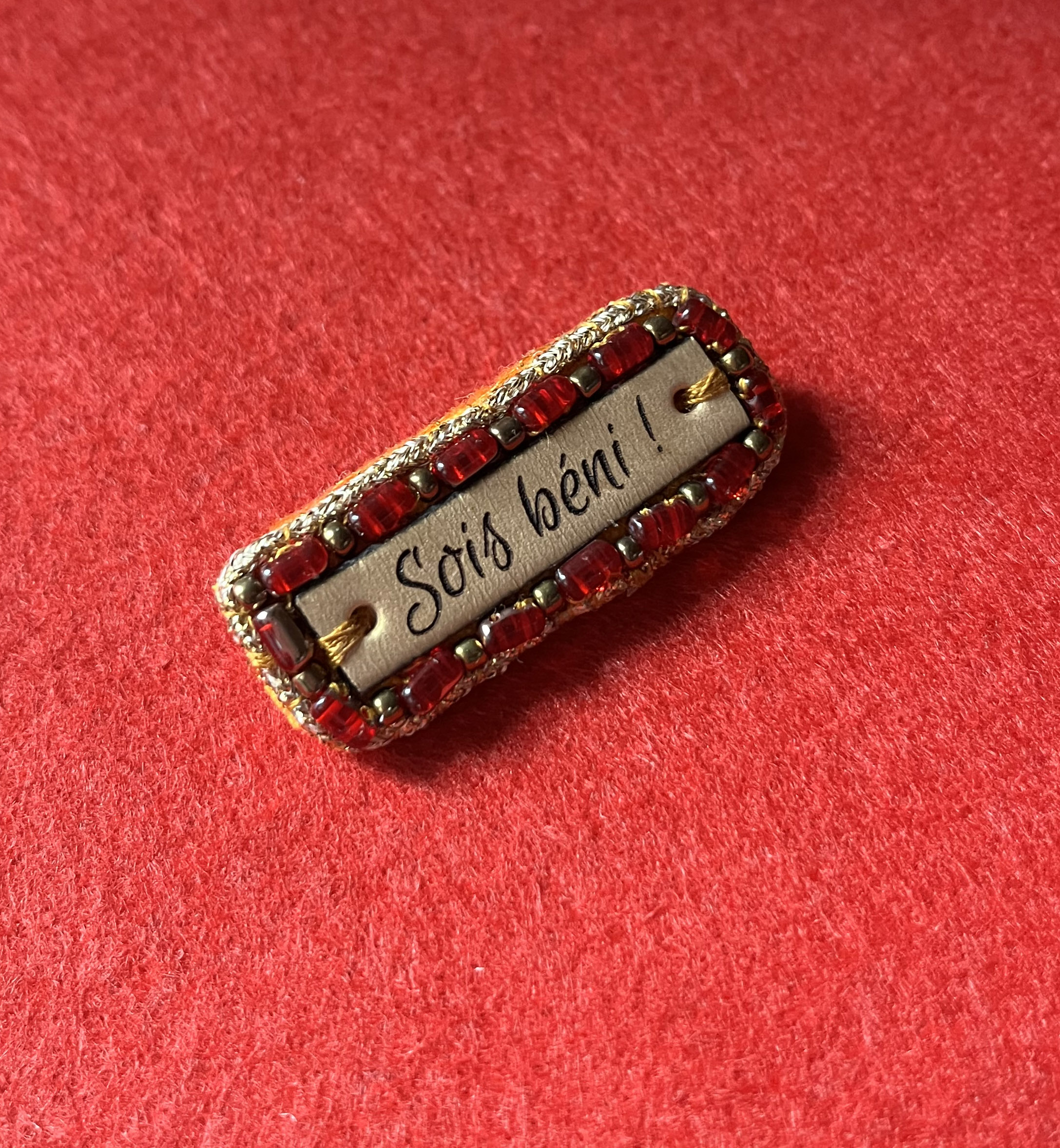 Broche à message en cuir gravé "sois béni" en perles rouges et dorées 