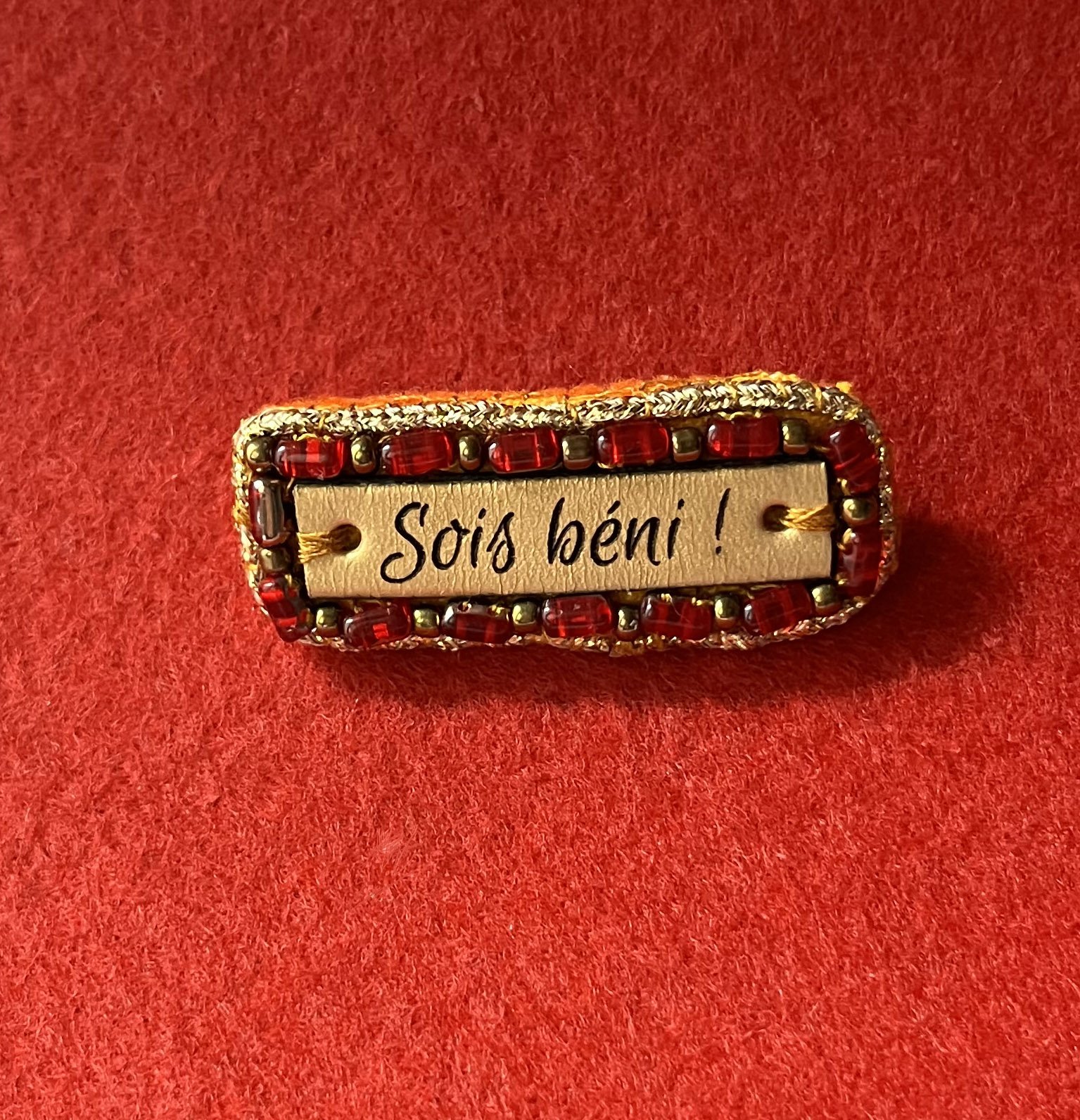 Broche à message en cuir gravé "sois béni" en perles rouges et dorées 