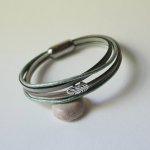 Bracciale in pelle multipla nei toni del beige, del verde chiaro e del perlato, decorato con una piccola piuma
